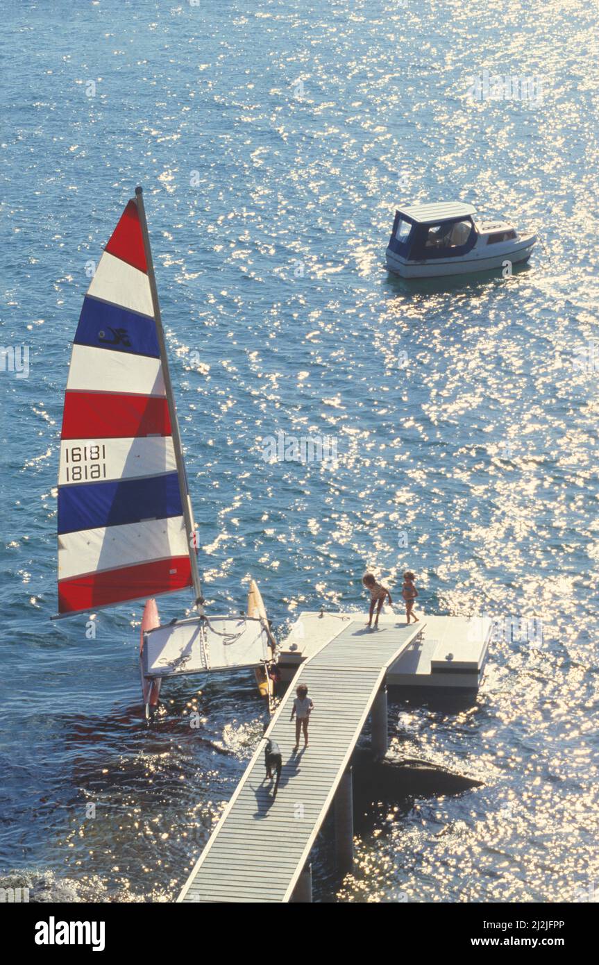 Australia. Sydney. Bambini sul jetty e catamarano Hobie Cat con vela sollevata. Foto Stock