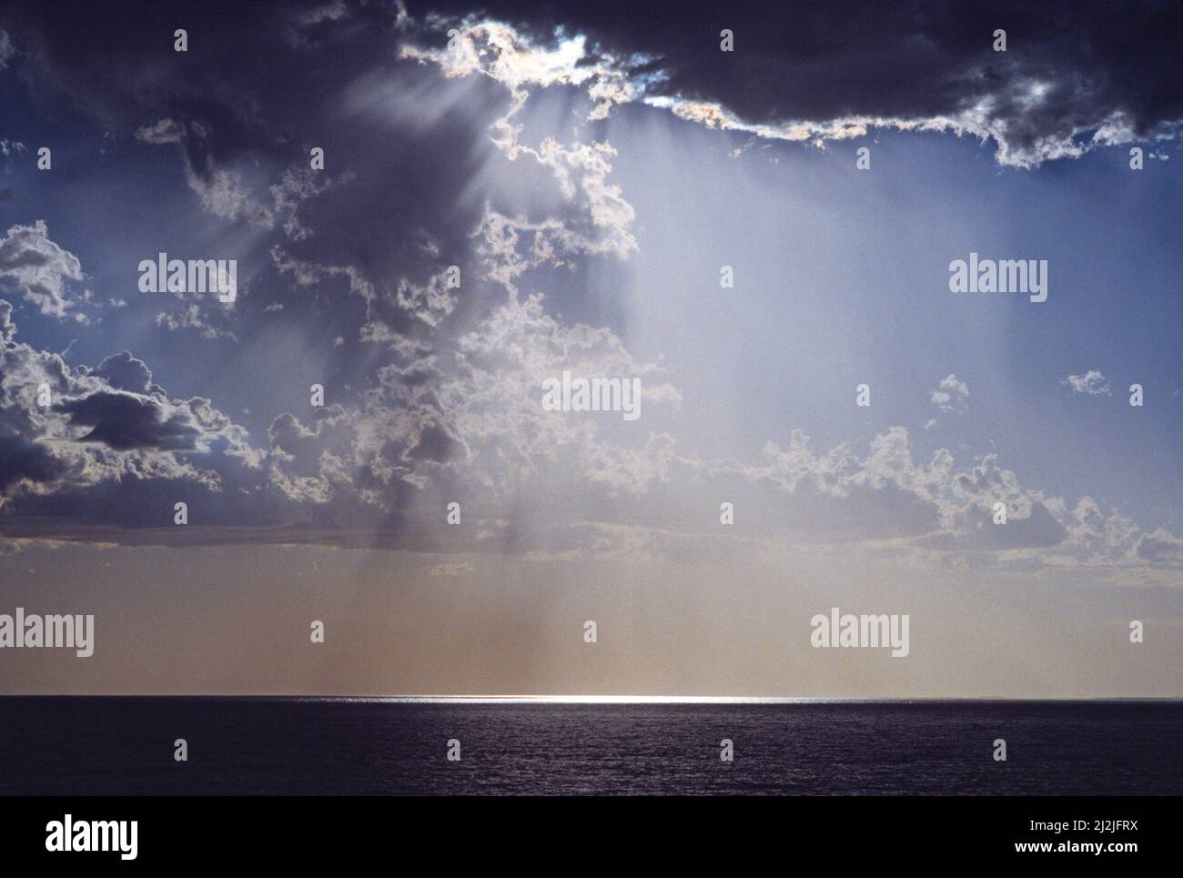 La luce del sole splende attraverso il cielo tempestoso sull'oceano. Foto Stock