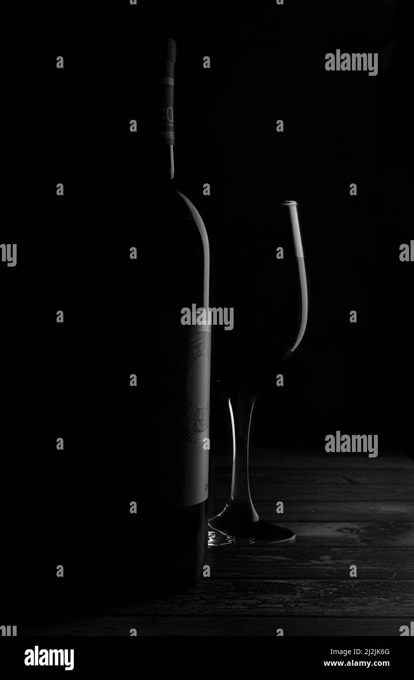 Fotografia scura in bianco e nero, una bottiglia di vino e una tazza di vetro su un tavolo rustico, illuminata da un bordo chiaro, scuro o nero, Foto Stock