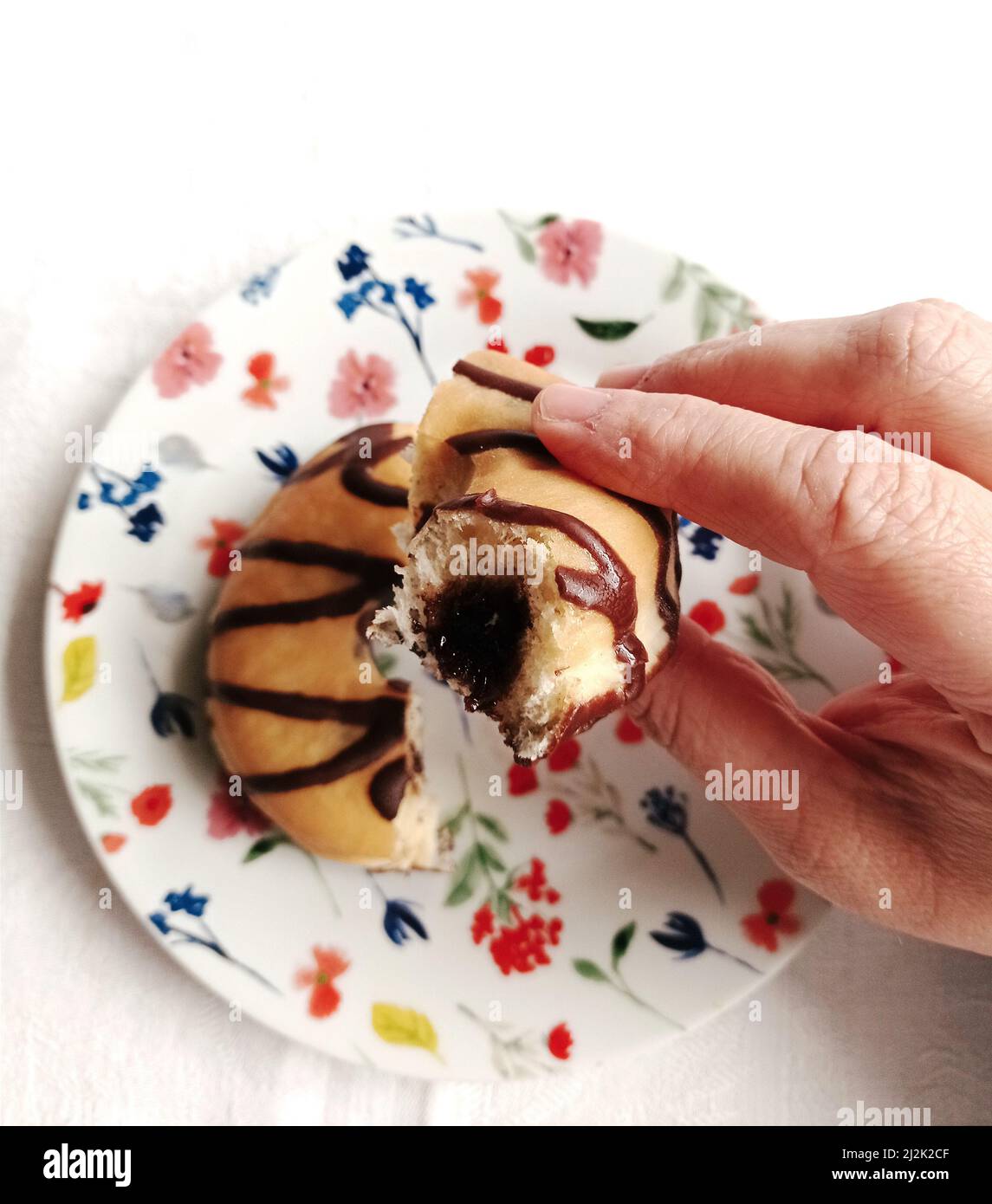 Mano della donna che tiene una ciambella ripiena di cioccolato mangiata a metà Foto Stock