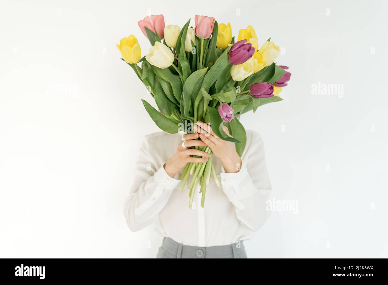 Donna che tiene un mazzo di tulipani multicolore davanti al suo viso Foto Stock