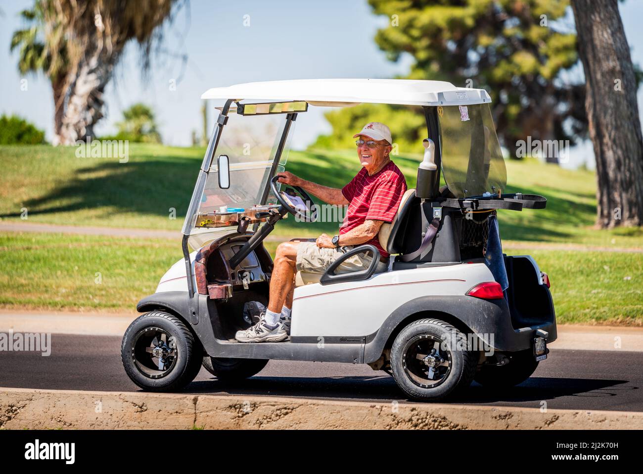 Uomo anziano che guida un golf cart vicino ad un campo a Sun City, Arizona, Stati Uniti Foto Stock