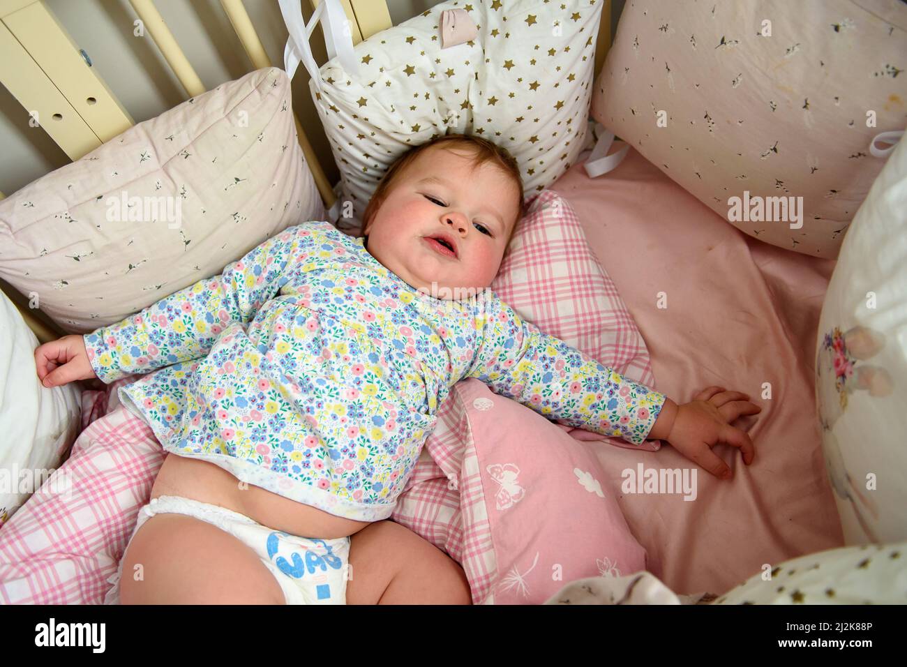 Ragazza carina di dieci mesi, giocando da sola in una culla a casa nel pomeriggio o al mattino Foto Stock