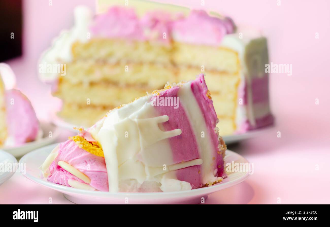 Spugna umida di madeira, ricoperta di confettura di prugne e lamponi, ricoperta di glassature bianche e rosa, decorata con deco di cioccolato bianco Foto Stock