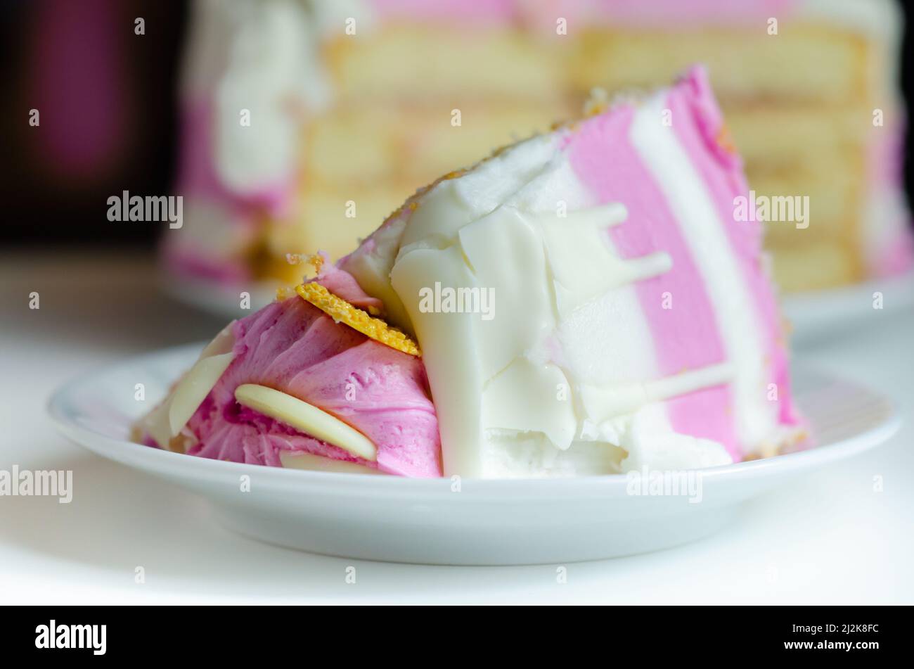 Spugna umida di madeira, ricoperta di confettura di prugne e lamponi, ricoperta di glassature bianche e rosa, decorata con deco di cioccolato bianco Foto Stock