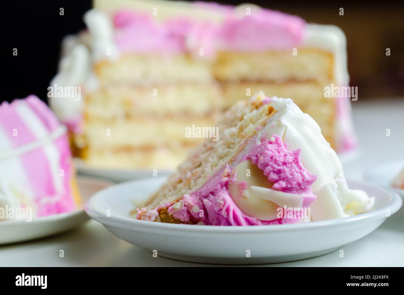 Spugna umida di madeira, ricoperta di confettura di prugne e lamponi, ricoperta di glassature bianche e rosa, decorata con deco di cioccolato bianco Foto Stock