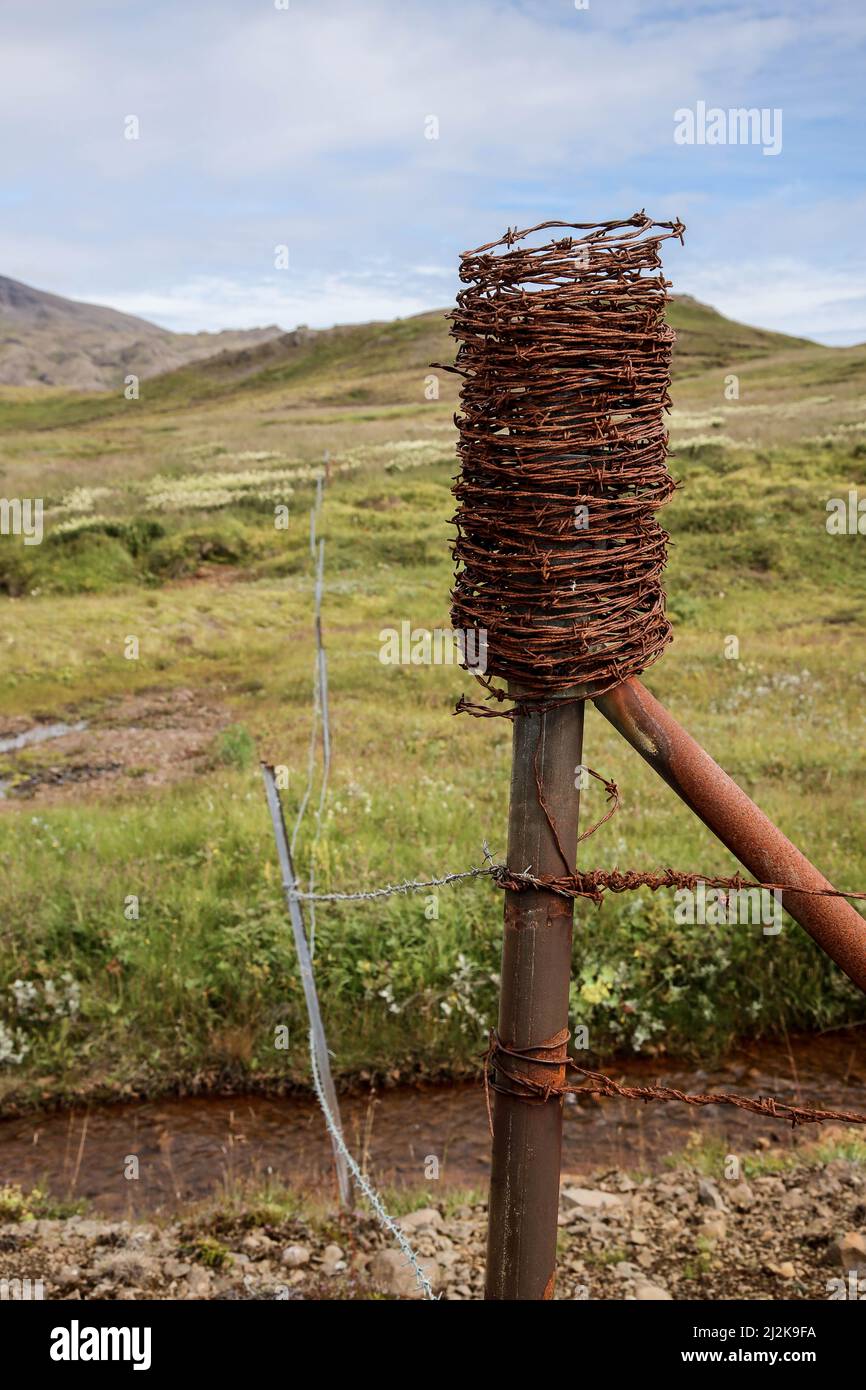 Un primo piano verticale di un palo metallico ricoperto di filo spinato contro colline verdi in Islanda Foto Stock