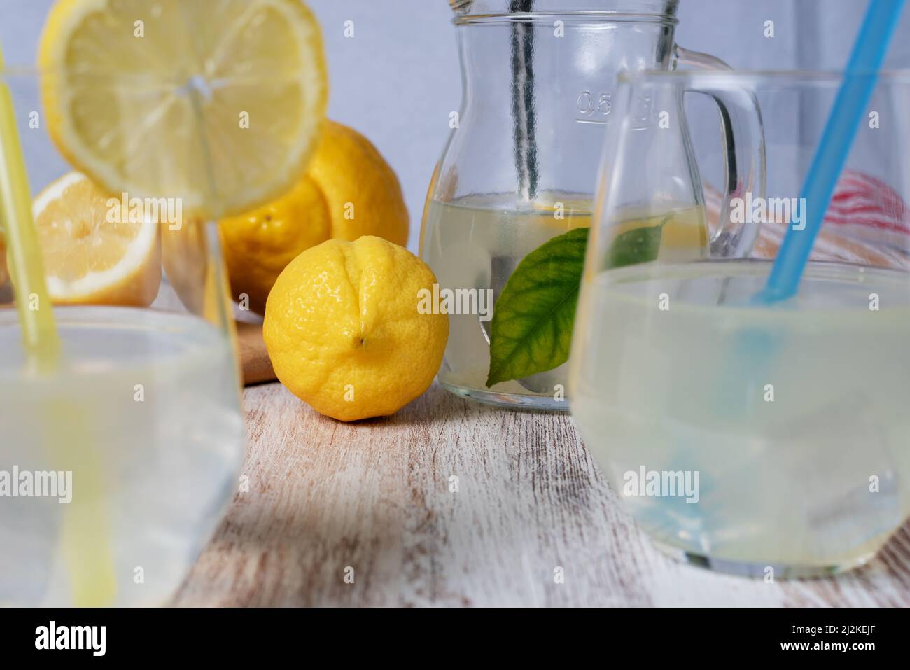 Limone accanto ad alcuni bicchieri con cannucce e una caraffa di limonata. Foto Stock