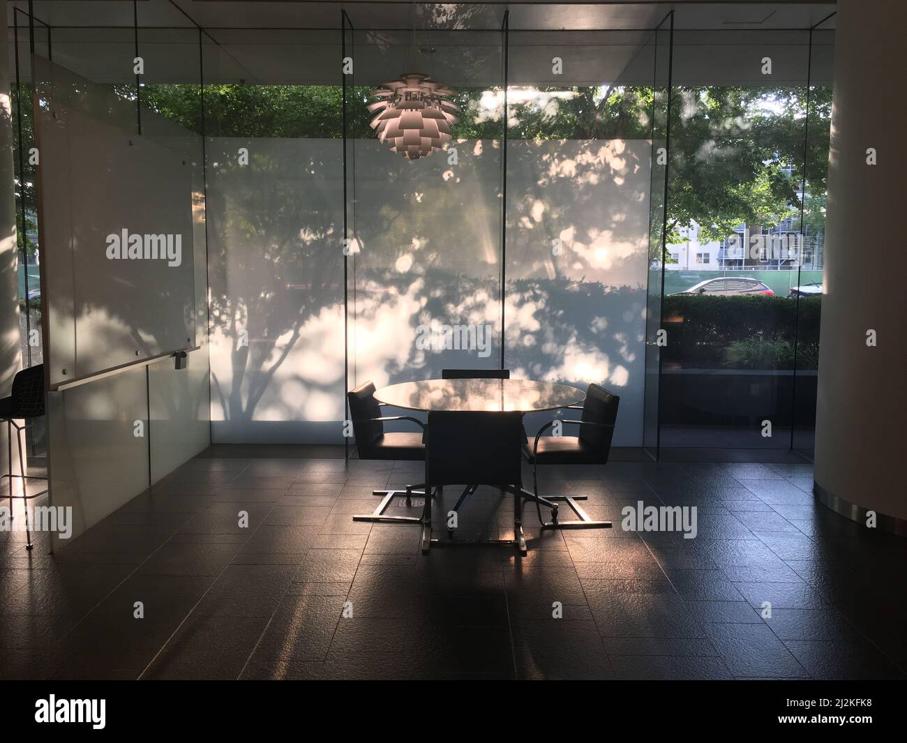 Un interno di un ufficio con pareti in vetro trasparente, un tavolo rotondo e sedie Foto Stock