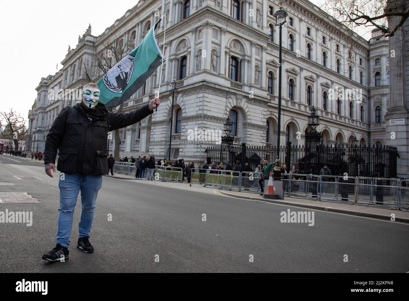 Londra, Regno Unito. 2 aprile 2022. Un uomo che indossa una maschera ondeggia una bandiera del gruppo hacktivist Anonymous fuori Downing Street dove la gente si è riunita per protestare contro il costo crescente di vivere nel paese. Credit: Kiki Streitberger/Alamy Live News Foto Stock