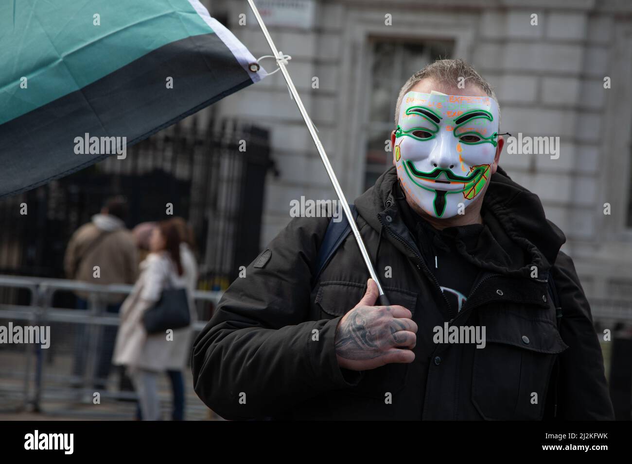 Londra, Regno Unito. 2 aprile 2022. Un uomo che indossa una maschera ondeggia una bandiera del gruppo hacktivist Anonymous fuori Downing Street dove la gente si è riunita per protestare contro il costo crescente di vivere nel paese. Credit: Kiki Streitberger/Alamy Live News Foto Stock