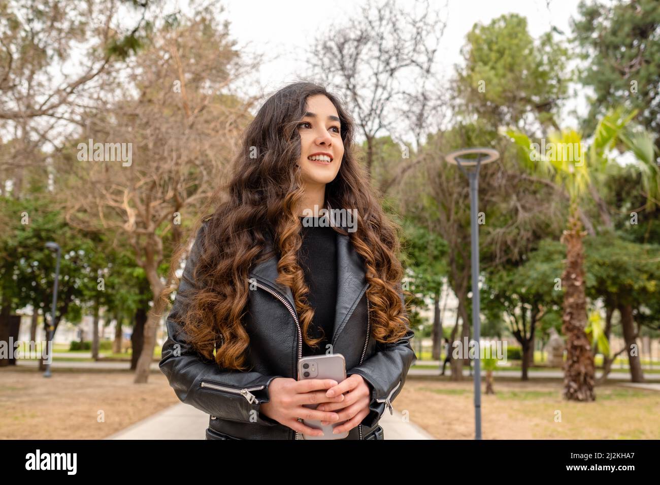 La giovane donna di successo si levano in piedi all'esterno tenendo il telefono sullo sguardo dello stomaco via con sorriso sicuro. Felice giovane donna razza femminile imprenditore privato Foto Stock