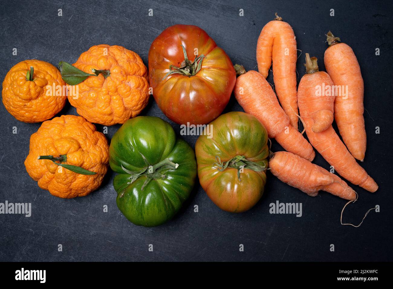 frutta brutta, verdura fresca biologica di pomodoro carota mandarino arancione sullo sfondo nero scuro vista dall'alto da vicino Foto Stock