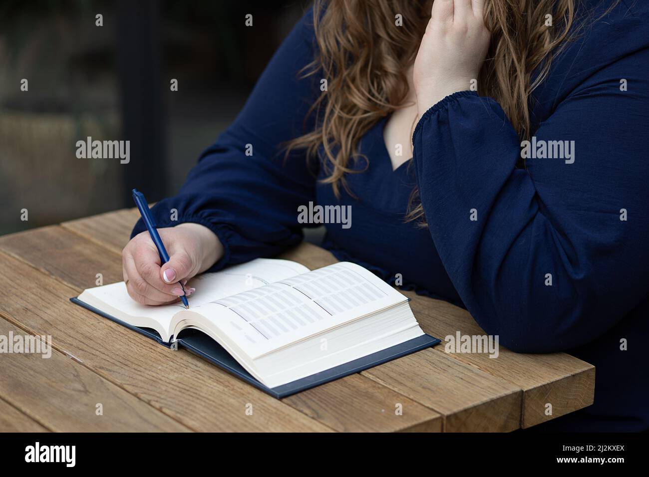 Closeup donna occupato scrittura e prendere appunti in notebook tenendo penna. Scrittura a mano sulla scrivania sul posto di lavoro, sfondo sfocato scuro, messa a fuoco selettiva, gratis Foto Stock