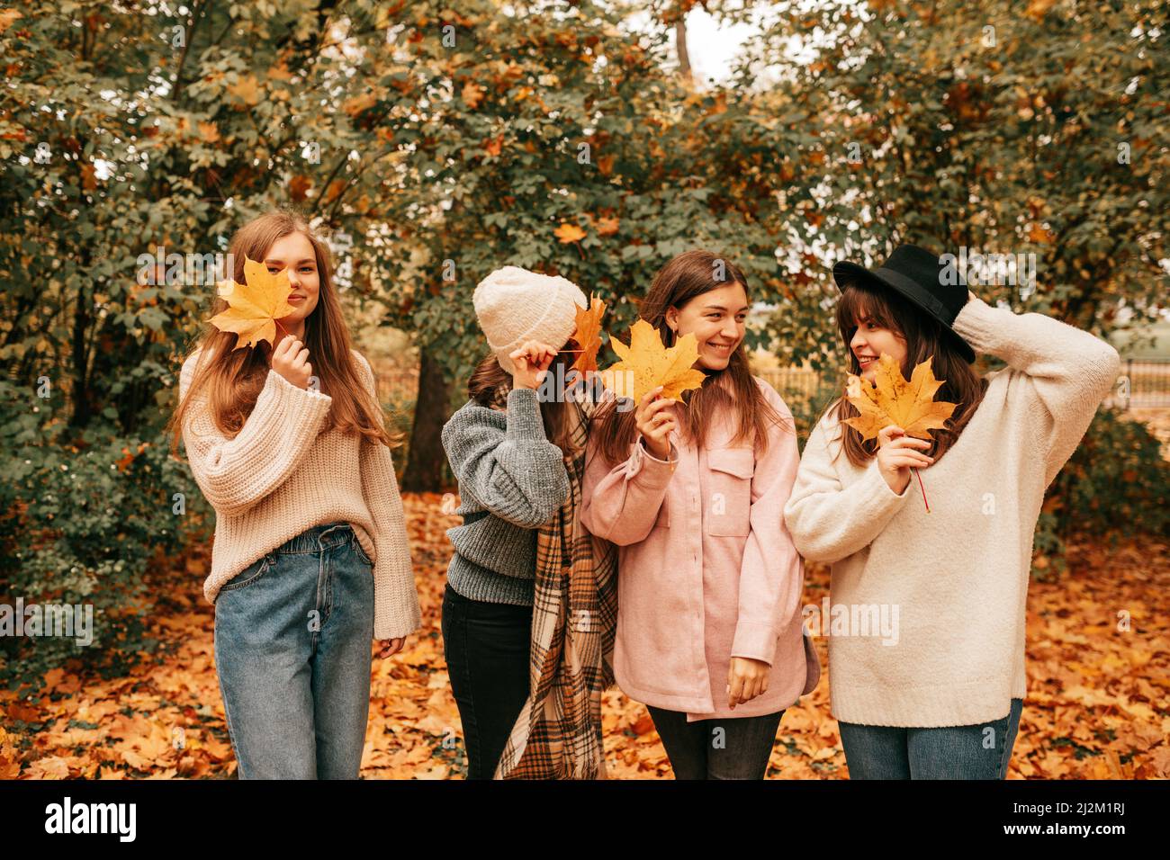 Quattro amici femmina vicino gruppo aziendale passare il tempo insieme, parlare, ingannare intorno, nascondere faccia, autunno. All'aperto Foto Stock