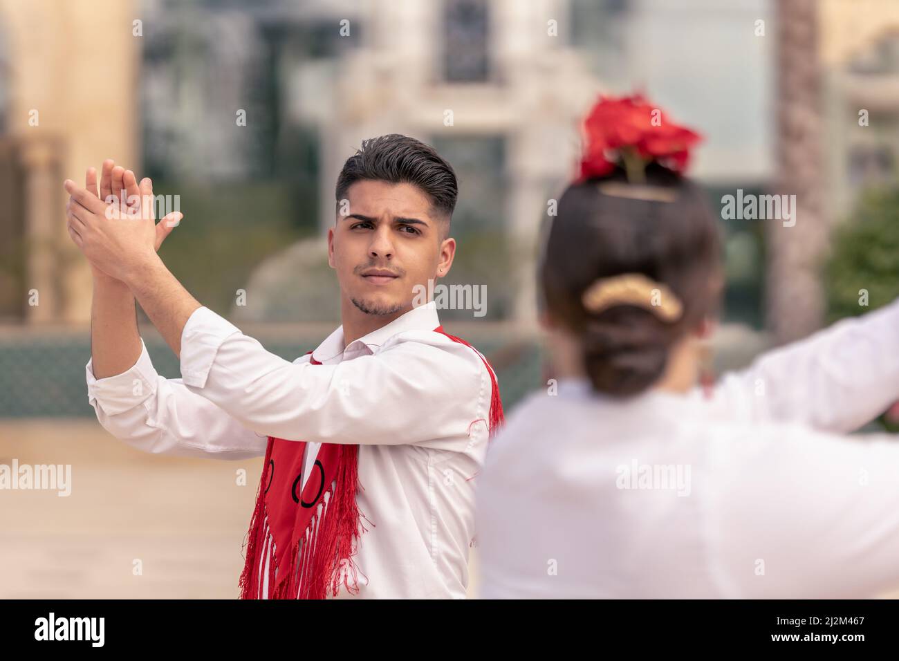 giovane ballerino maschile in un mantillo rosso che stringe le mani mentre balla flamenco con il suo compagno per strada Foto Stock