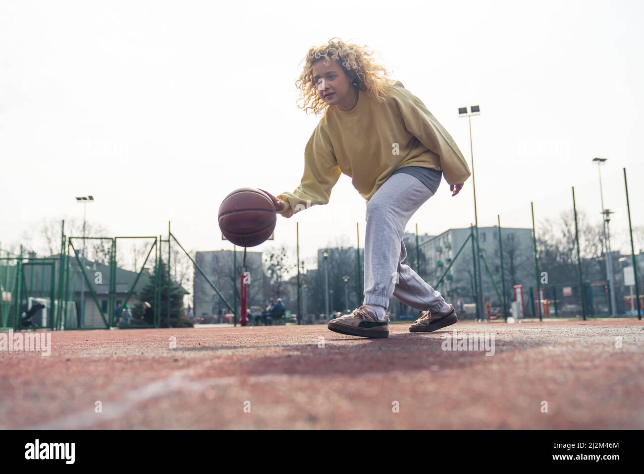 Bella bionda capelli ricci donna giocare a basket sul campo sportivo da solo, copia spazio full shot . Foto di alta qualità Foto Stock