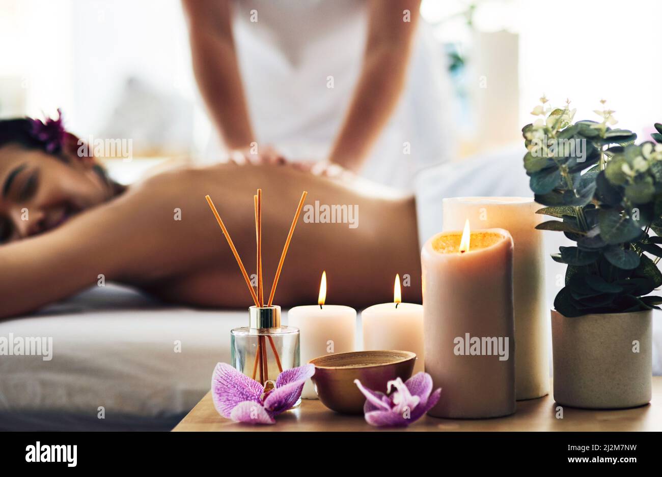 È tempo di rallentare le cose. Shot di elementi essenziali per il centro benessere su un tavolo con una donna che riceve un massaggio sullo sfondo. Foto Stock