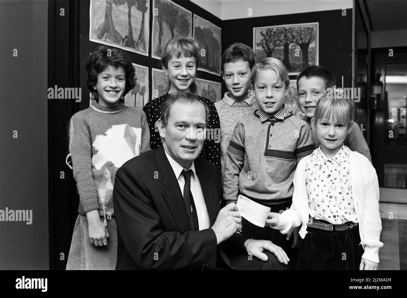 I bambini danno in denaro per beneficenza. I bambini sono andati senza soldi della tasca e hanno fatto i lavori supplementari intorno alle loro case per aiutare una carità che funziona per i giovani con cancro. Mike Emery, presidente della Candlelighters, con sede presso il St James' Hospital di Leeds, riceve un assegno per £400 persone da Cassandra Darwin (destra), dalla Highburton CE First School e da altri allievi (da sinistra) Olivia Preston, Claire Armstrong, David Turnbull, Dominik Sobanski e John Gill. 31st ottobre 1989. Foto Stock