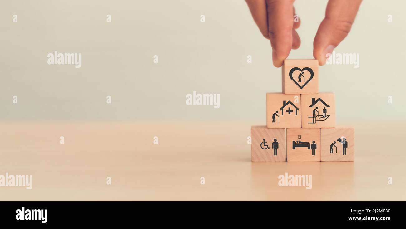 Concetto di assistenza agli anziani. La mano tiene i cubi di legno con le icone relative alla cura anziana, al medico, al servizio di riabilitazione, all'assistenza infermieristica per migliorare la qualità Foto Stock