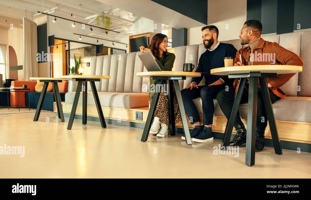 Team di uomini d'affari che lavorano in una lobby d'ufficio. Tre uomini d'affari felici sorridendo mentre hanno una discussione. Gruppo di imprenditori moderni collabora Foto Stock