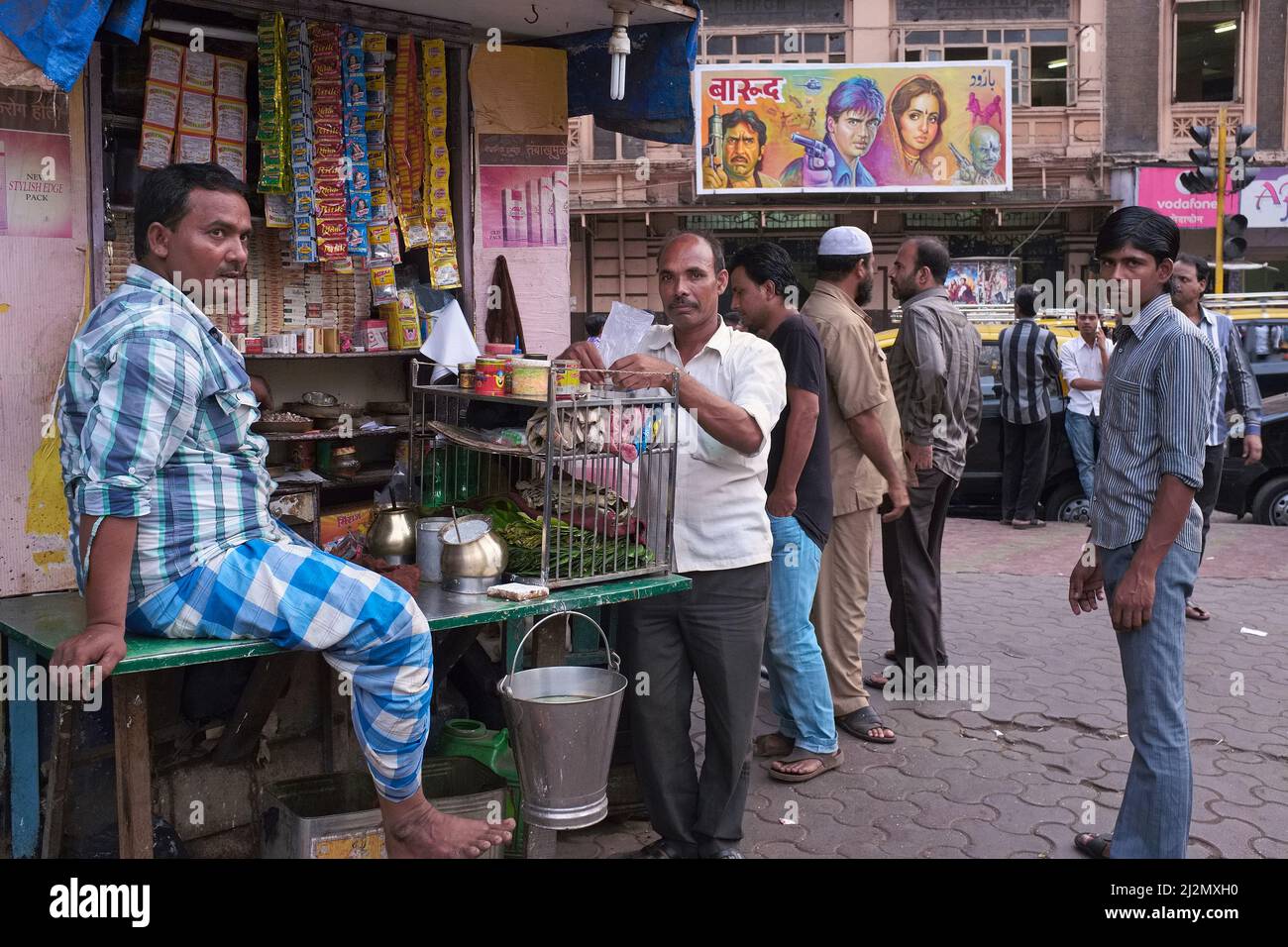 Gli uomini si levano attorno ad una bancarella di betel a Patthe Bapurao Marg, Khetwadi, Mumbai, India, un'area conosciuta per i suoi bordelli e cinema a buon mercato; b/g: Alfred Cinema Foto Stock