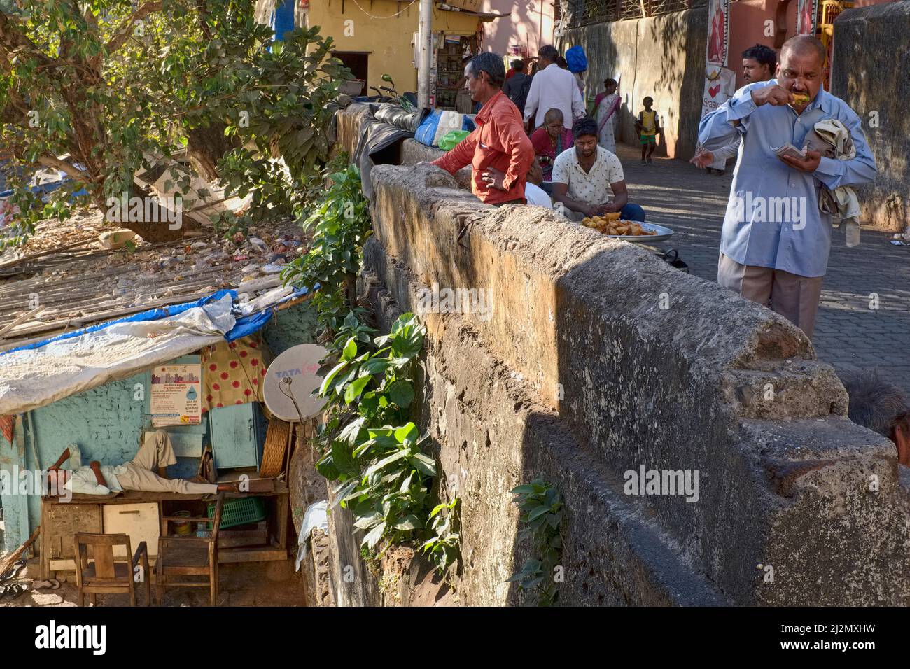 Una scena di pellegrinaggio sacro luogo Banganga serbatoio a Walkeshwar, Mumbai, India, un uomo che dorme all'ombra di una capanna, mentre un uomo vicino gode di uno spuntino Foto Stock