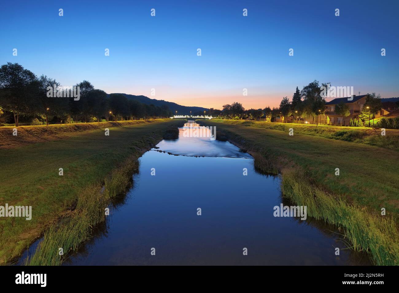 Erba verde sulle rive del fiume accanto al flusso d'acqua del fiume Nisava al crepuscolo nella città di Pirot, Serbia Foto Stock