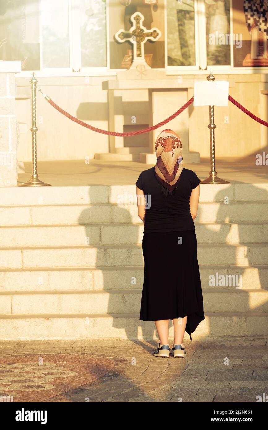 Ostrog Monastery, donna pellegrina con velo sta pregando di fronte ad una croce ortodossa - Montenegro Foto Stock