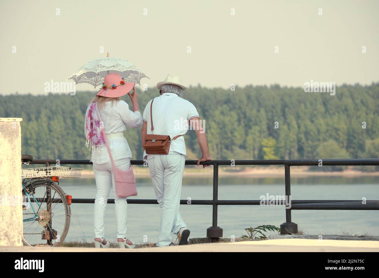 Coppia di mezza età in bianco vestito con i cappelli al mattino caldo sulla banchina del Danubio a Vidin; la signora si protegge dal sole con una retrò la Foto Stock