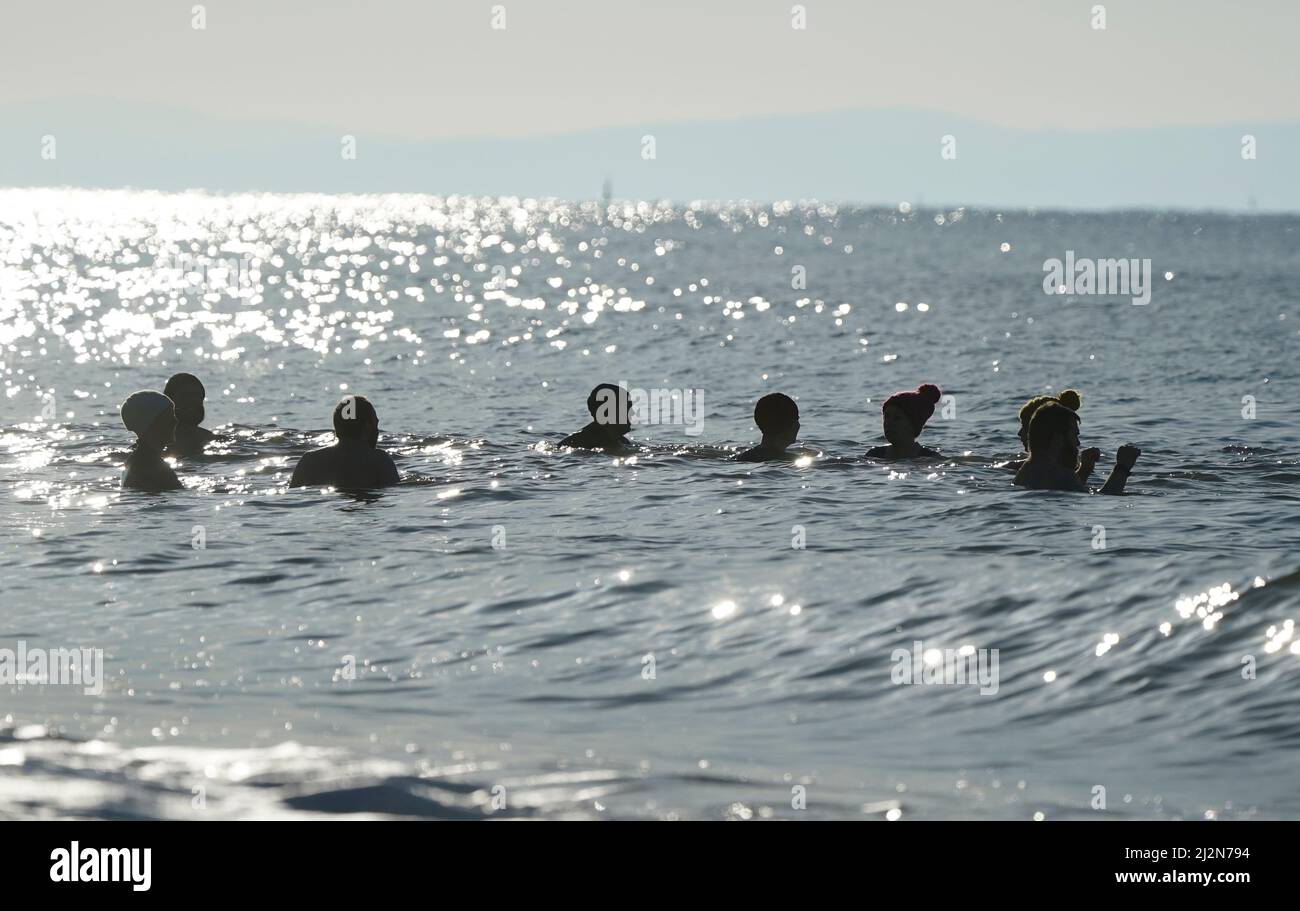 La gente nuota in mare al largo della spiaggia di Boscombe nel Dorset. Data foto: Domenica 3 aprile 2022. Foto Stock