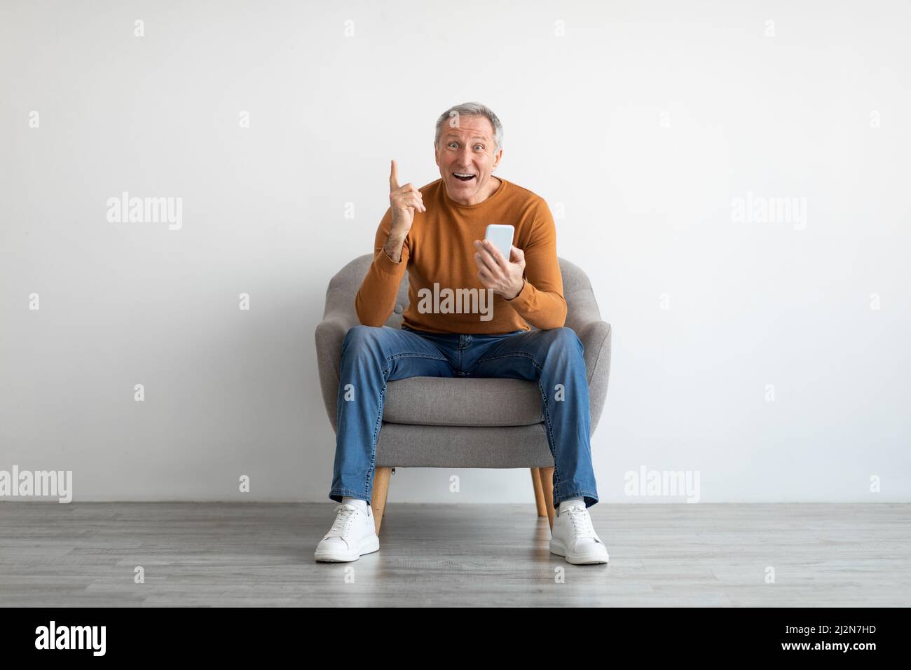 Ritratto di uomo maturo con smartphone seduto su poltrona Foto Stock