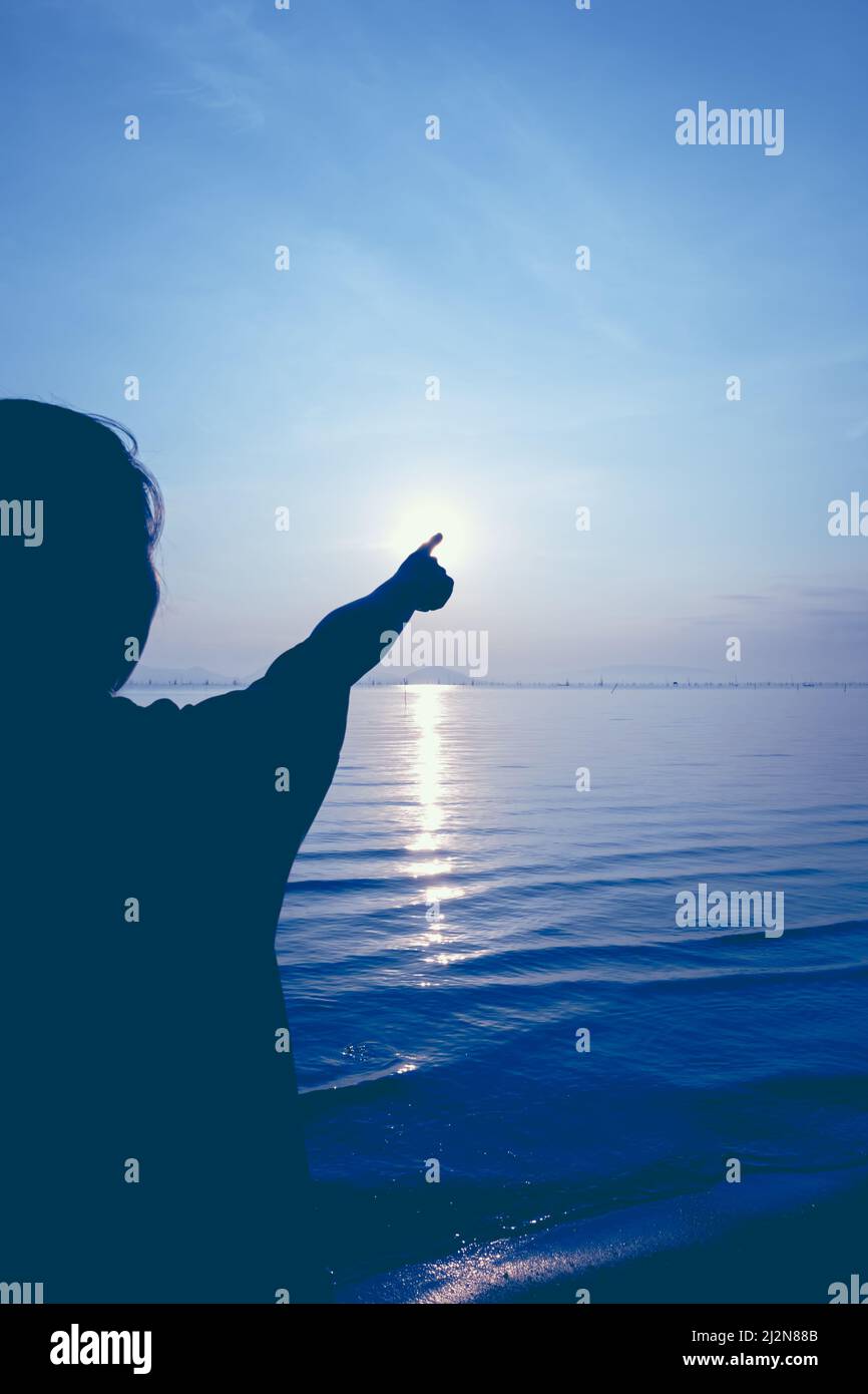 Silhouette vista posteriore della donna relax al mare e puntare al sole su sfondo blu colorato cielo. Stile immagine vintage. All'aperto. Foto Stock