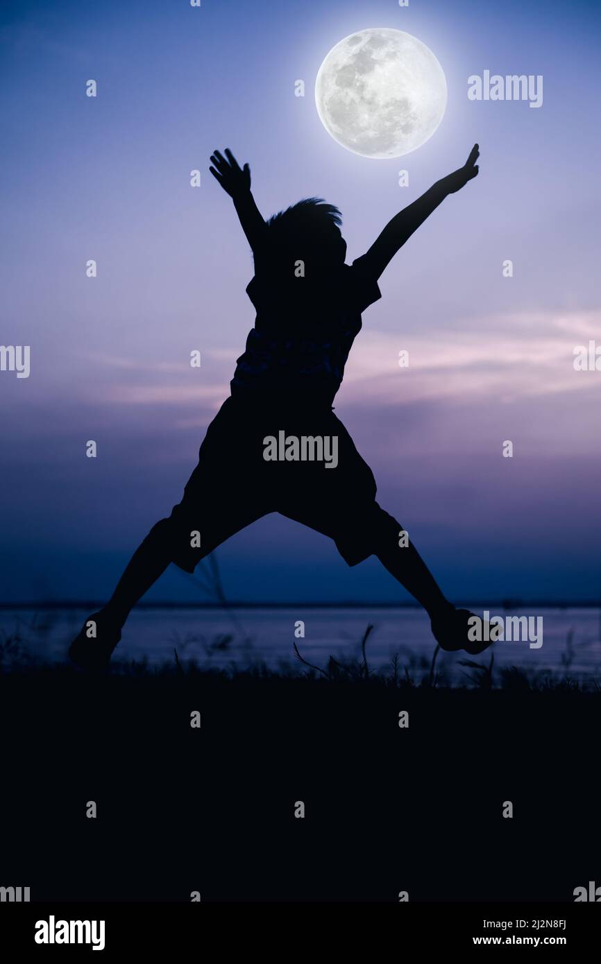 Vista posteriore della silhouette del bambino che si diverta e salta lungo il fiume. Luna piena con fantastico sfondo cielo. Buon tempo in vacanza. All'aperto. Colori freddi Foto Stock