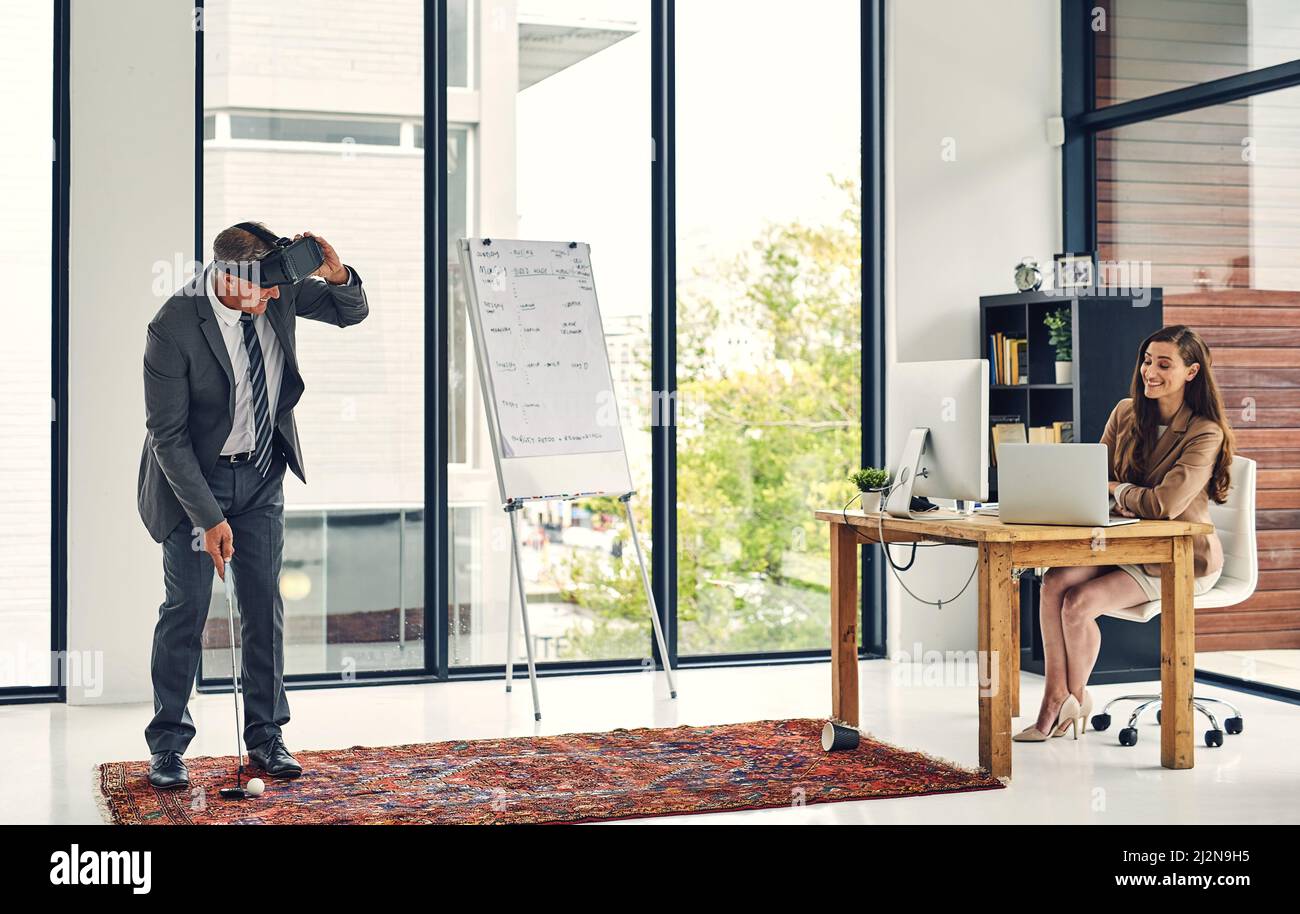 Questo sarà un colpo buco-in-one. Scatto di una donna d'affari che guarda il suo collega giocare a golf indossando un visore VR in ufficio. Foto Stock