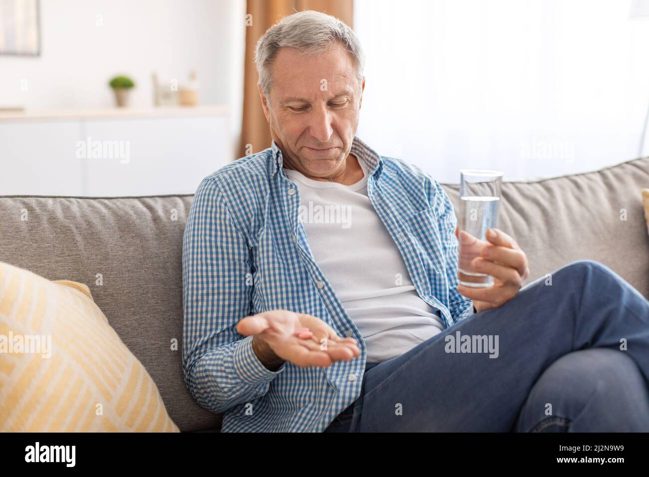 Uomo maturo che prende le pillole che tengono un bicchiere d'acqua Foto Stock