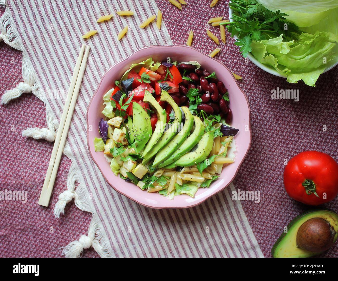 Ciotola sana con avocado, verdure e pasta su foderata bianca, fondo rosso e piatto rosa Foto Stock