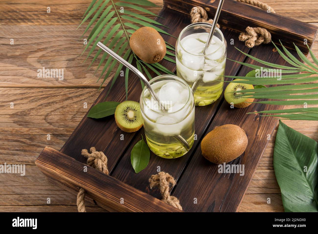 due bicchieri moderni sotto forma di lattina di birra con una bibita dolce e sana di kiwi e pezzi di ghiaccio su un vassoio di legno Foto Stock