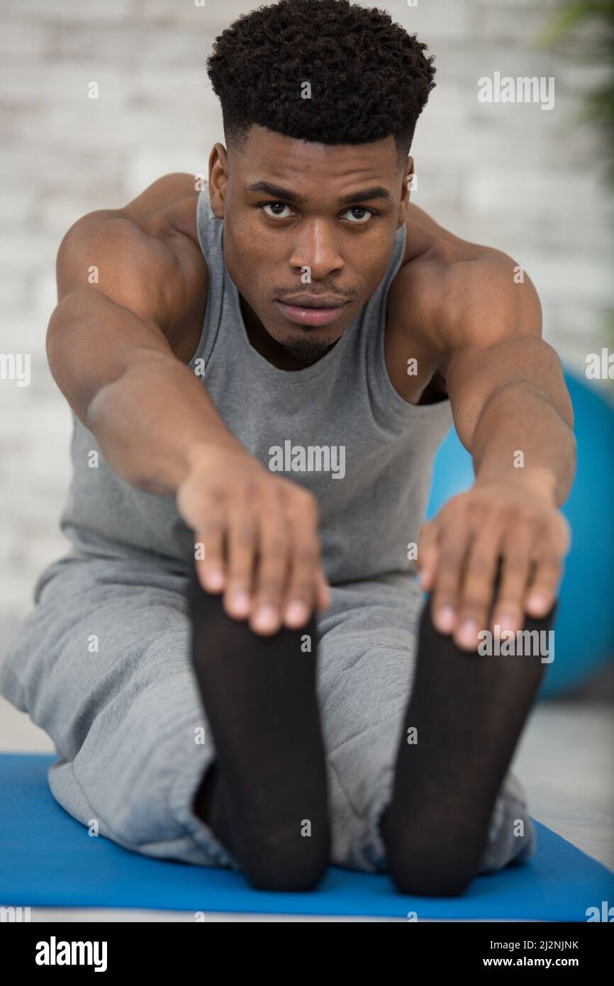 giovane uomo su tappeto che si allunga in avanti e tiene le dita dei piedi Foto Stock