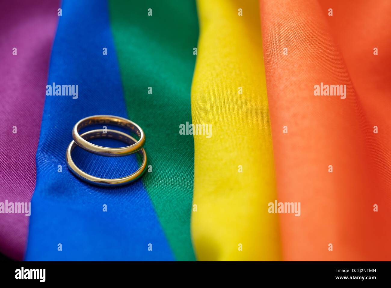 Matrimonio gay LGBT. Coppia di anelli dorati su tessuto color arcobaleno con pieghe, vista ravvicinata. Spazio di copia. Foto Stock