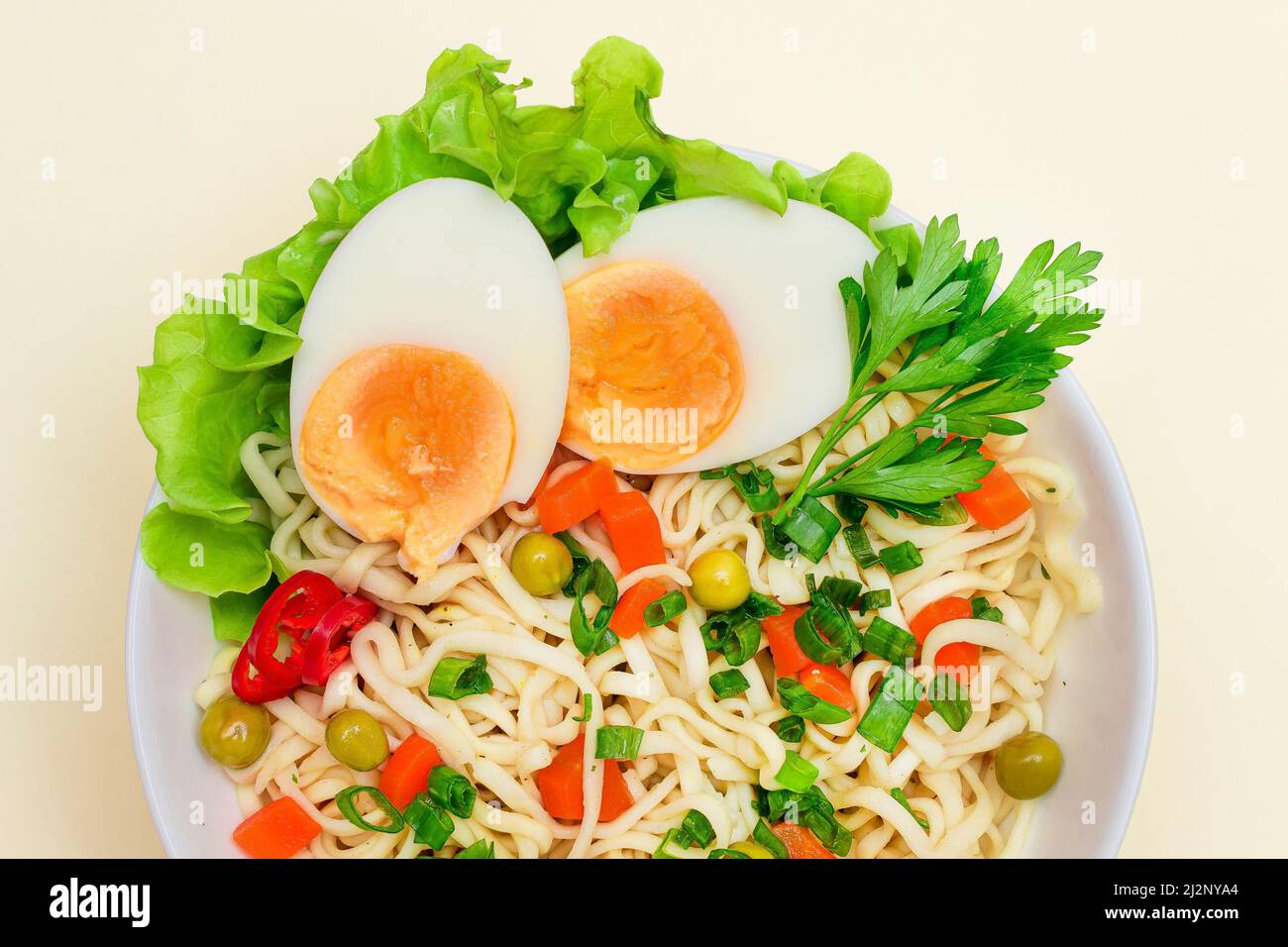 Bella pasta con piselli verdi, carota, uova, peperoncino rosso e verdi su sfondo bianco. Tagliatelle istantanee con verdure Foto Stock