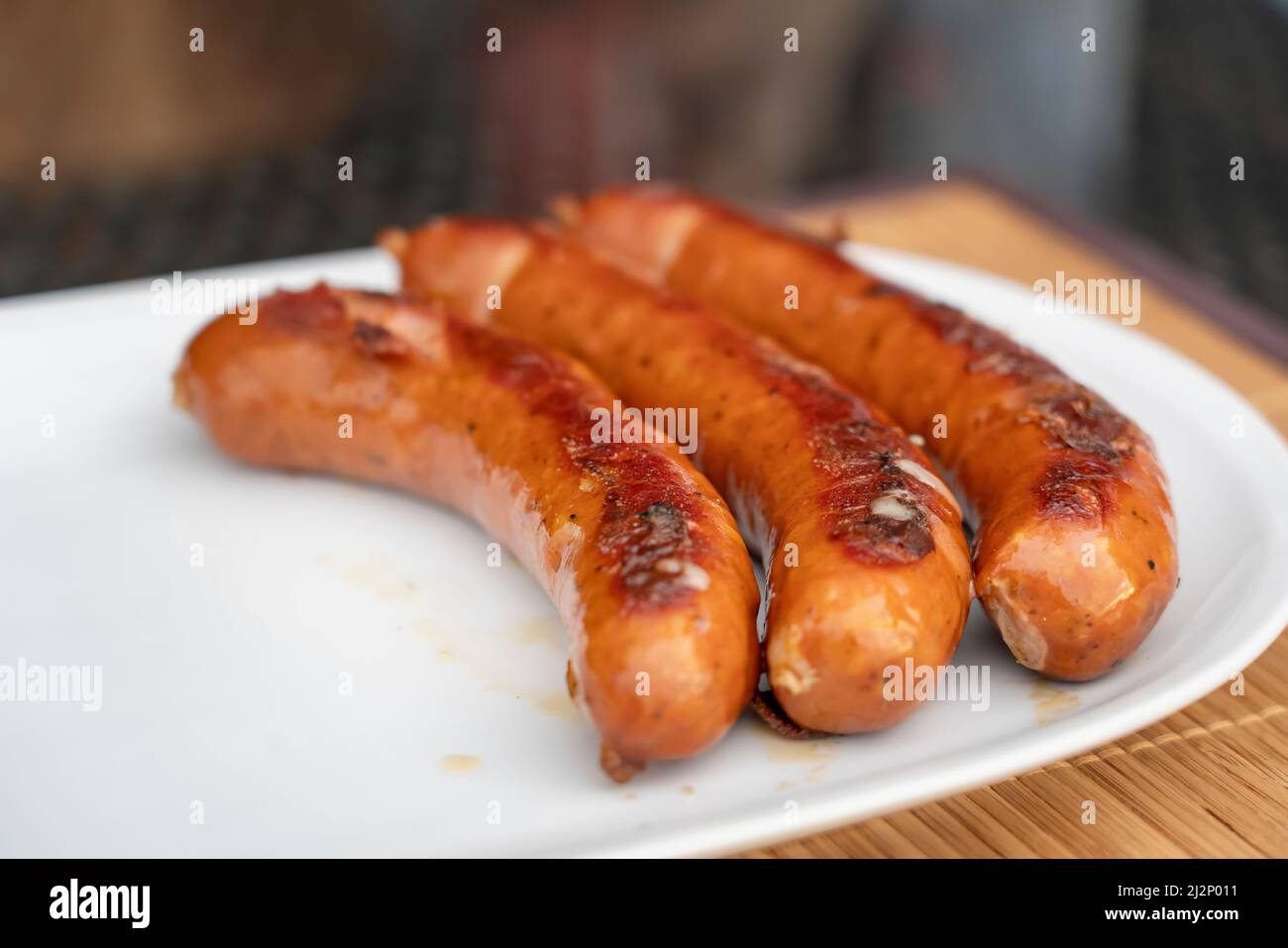 Barbecue a base di salsiccia Juicy Burned Sizzle on con sale e peperoni neri sul piatto bianco per pranzo barbecue grigliato per picnic in estate. Bratwurst o Hot Dogs on Foto Stock