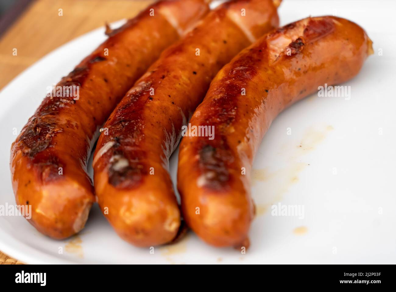 Barbecue a base di salsiccia Juicy Burned Sizzle on con sale e peperoni neri sul piatto bianco per pranzo barbecue grigliato per picnic in estate. Bratwurst o Hot Dogs on Foto Stock
