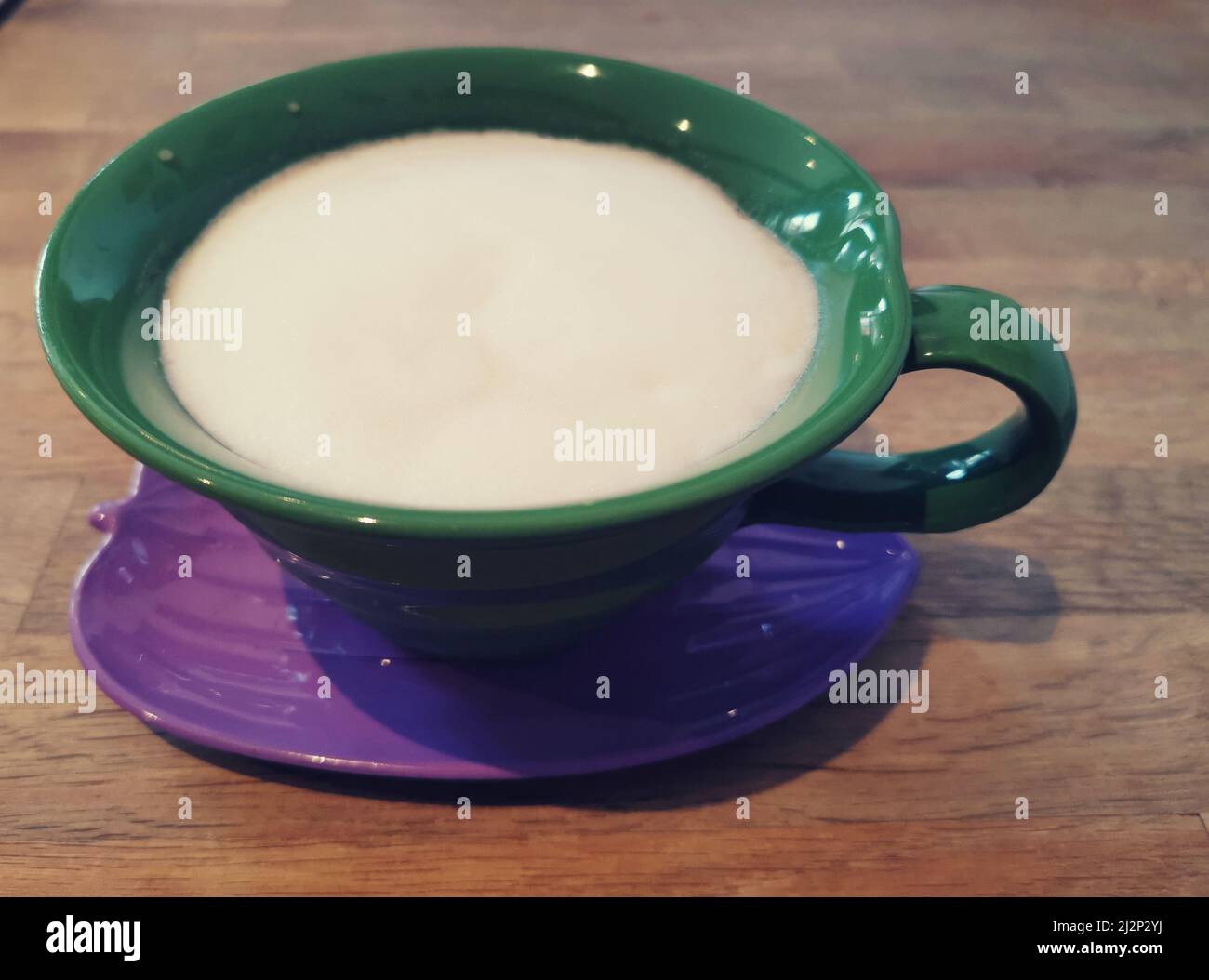Caffè servito in tazza verde e piattino viola sul tavolo Foto Stock