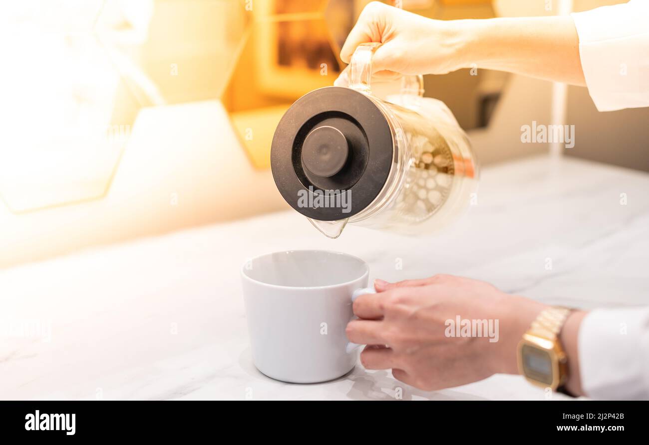Tenere una tazza bianca mentre si prepara a versare l'acqua con lo sfondo bianco. Foto Stock