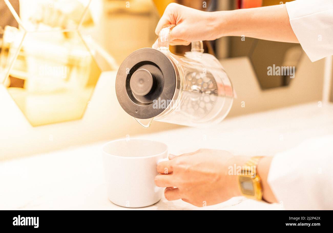 Tenere una tazza bianca mentre si prepara a versare l'acqua con lo sfondo bianco. Foto Stock