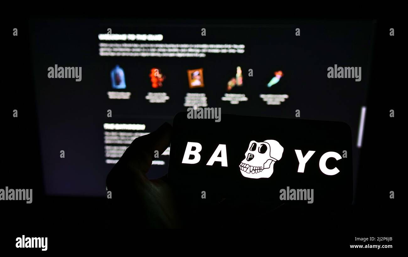 Persona che tiene il telefono cellulare con il logo di Ape Yacht Club annoiato (BAYC, Yuga Labs) sullo schermo di fronte alla pagina web del business. Mettere a fuoco sul display del telefono. Foto Stock