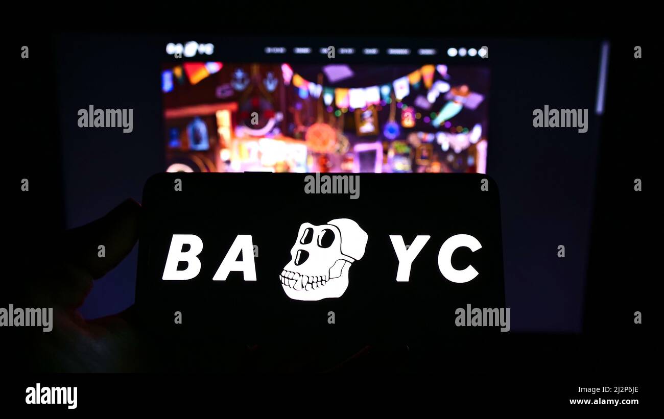 Persona che tiene il cellulare con il logo di Ape Yacht Club annoiato (BAYC, Yuga Labs) sullo schermo di fronte al sito web aziendale. Mettere a fuoco sul display del telefono. Foto Stock