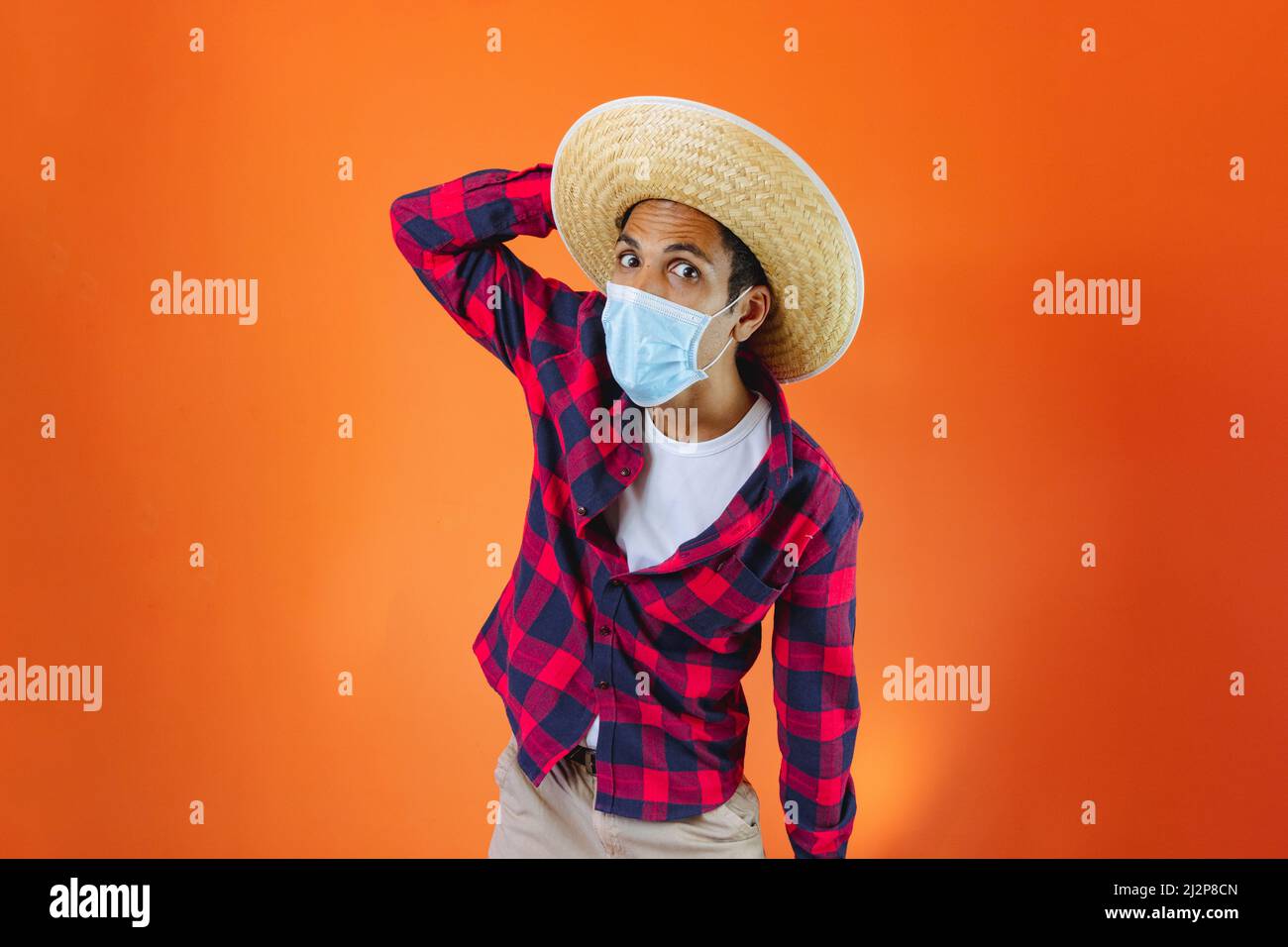 Black Man con Junina Party vestito e maschera pandemica isolato su sfondo arancione. Giovane uomo che indossa abiti tradizionali per Festa Junina - Brasiliano Foto Stock