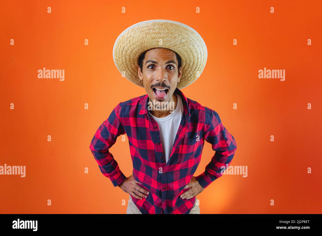 Black Man con Junina Party vestito isolato su sfondo arancione. Giovane uomo che indossa abiti tradizionali per Festa Junina - Festival brasiliano di giugno. Foto Stock